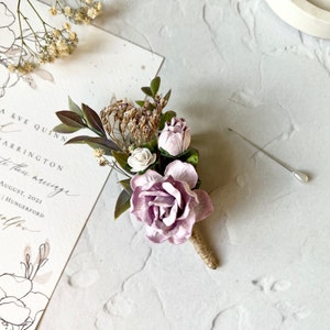 May include: A small bouquet of purple and white flowers with dried flowers and greenery. The bouquet is attached to a piece of twine and a pin is included.