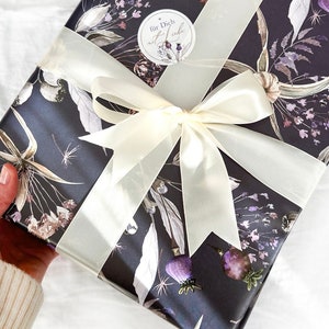 May include: A gift wrapped in dark blue paper with a floral pattern. The paper has a white ribbon tied in a bow. A white sticker with the text "f&uuml;r Dich mit Liebe" is on the box.