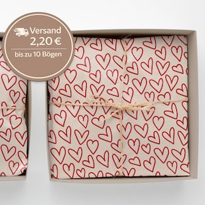Könnte beinhalten: Zwei Geschenkboxen mit Geschenkpapier mit einem Muster aus roten Herzen auf cremefarbenem Hintergrund. Jede Box ist mit Bindfaden gebunden. Die Boxen befinden sich in einer hellgrauen Box.