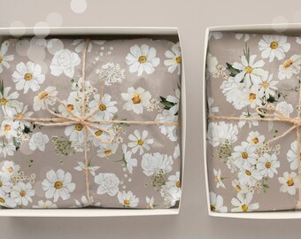 May include: Two gift boxes wrapped in brown paper with a white daisy floral pattern. The boxes are tied with twine and have a simple, elegant design.