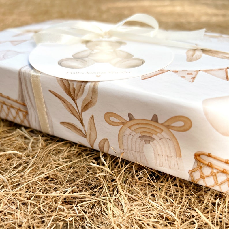 Op de afbeelding: Een witte cadeaudoos met een bruin en wit patroon. De doos is vastgebonden met een wit lint en heeft een rond label met de tekst "Hallo, kleine Wunder".