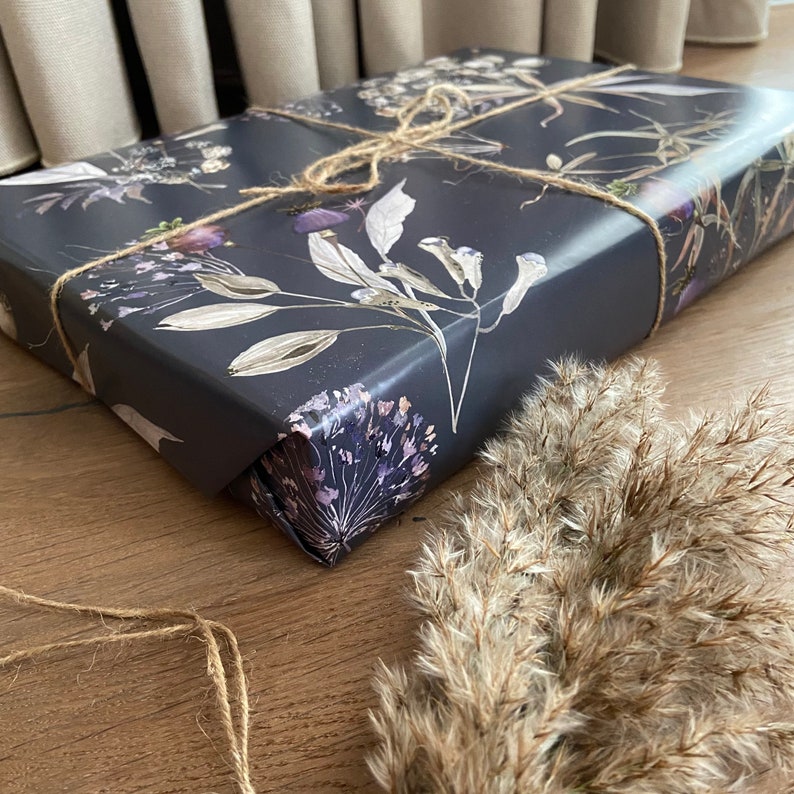 May include: Dark grey gift wrap with a floral pattern featuring dried flowers and leaves. The wrapping paper is tied with twine.