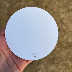 Op de afbeelding: Een ronde witte kaart met de tekst "mit Liebe" en een klein hartje.