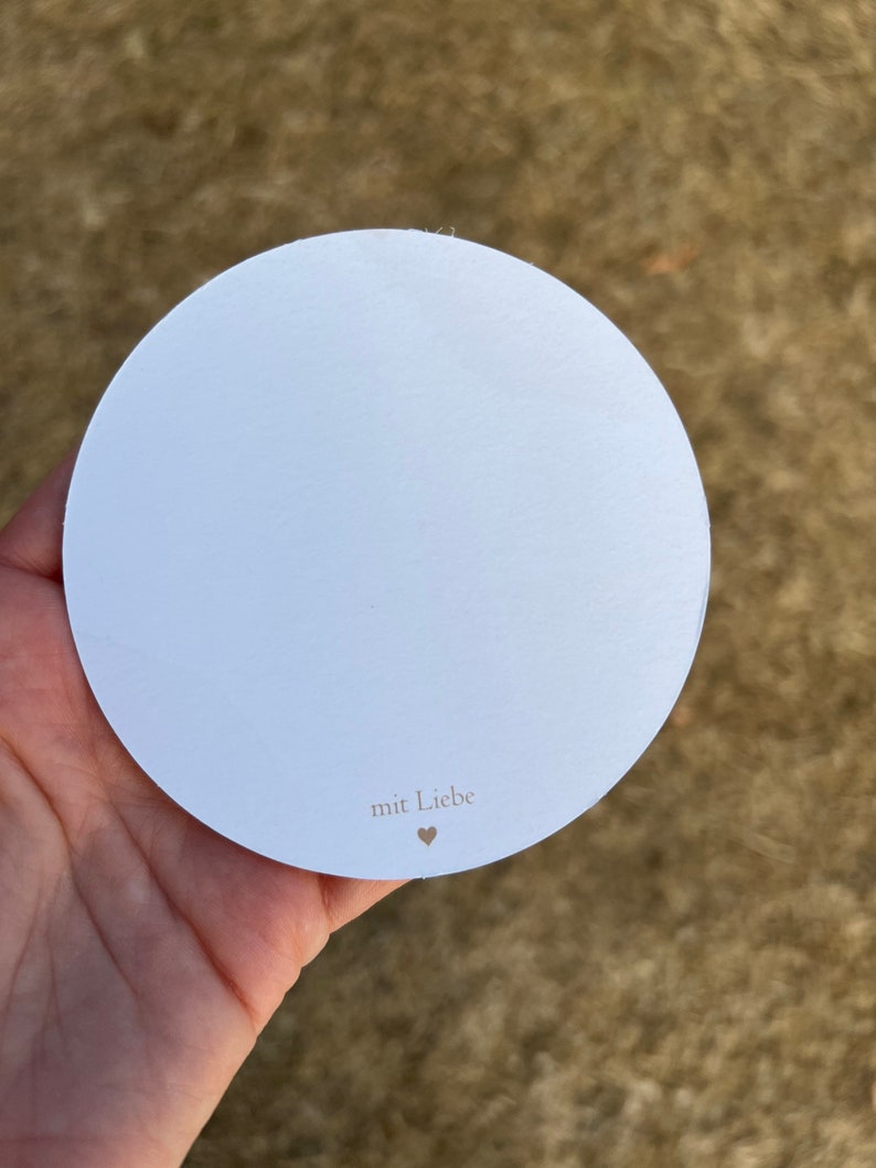 Op de afbeelding: Een ronde witte kaart met de tekst "mit Liebe" en een klein hartje.