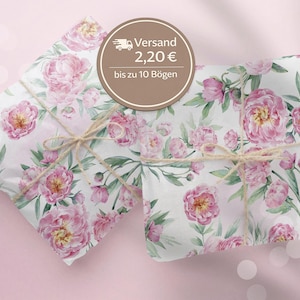 Könnte beinhalten: Zwei Geschenkpakete mit floralem Pfingstrosen-Design. Das Geschenkpapier zeigt rosa Pfingstrosen und grüne Blätter auf weißem Hintergrund. Die Pakete sind mit Bindfaden verschnürt.