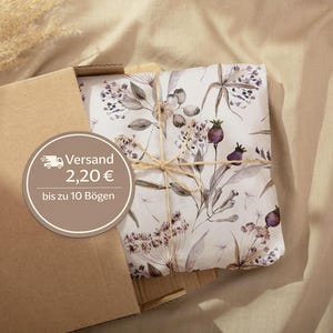 Peut inclure: Un colis emballé dans du papier à motifs floraux, ficelé avec de la ficelle, à l'intérieur d'une boîte en carton marron. Le motif floral présente des tons sourds de violet, de gris et de vert sur fond blanc. La boîte est ouverte, révélant le colis.