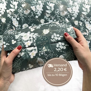 Könnte beinhalten: Dunkelgrünes Geschenkpapier mit einem floralen Muster aus weißen Blüten und grünen Blättern. Das Papier ist um ein rechteckiges Paket gewickelt. Der Text "FÜR DICH MIT LIEBE" ist auf dem Paket zu sehen.