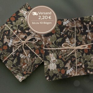 Könnte beinhalten: Zwei verpackte Geschenke mit dunklem Hintergrund. Das Geschenkpapier zeigt ein sich wiederholendes Muster aus Hirschen, Kaninchen, Pilzen und Beeren in Braun-, Grün- und Weißtönen. Jedes Paket ist mit Bindfaden gebunden.