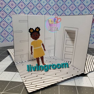 Pode incluir: Um diorama de casa de bonecas de papel com uma boneca de menina negra em pé em uma sala de estar. A boneca tem laços amarelos no cabelo e usa um vestido amarelo. A sala de estar tem uma porta, prateleiras e um piso com padrão preto e branco.