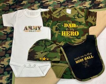 May include: A four-piece baby outfit set in a camouflage pattern. The set includes a white bodysuit with the text "ARMY BRAT", a camouflage bodysuit with the text "MY DAD IS MY HERO", a camouflage hat, and a black bib with the text "POINT ME TO THE MESS HALL".