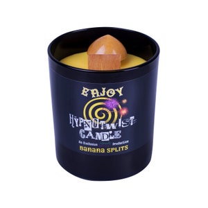 Op de afbeelding: Een zwarte kaars pot met een gele was top en een houten lont. Het etiket luidt "Enjoy HypnoTwist Candle An Exclusive Vanilla Production Banana Splits".