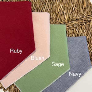 May include: Four fabric swatches in Ruby, Blush, Sage, and Navy. Each swatch is a different solid color with white stitching along the edges. The names of the colors are written on the fabric.