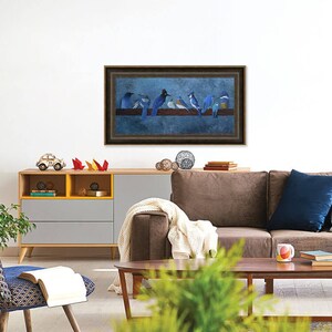 May include: A framed artwork featuring a group of blue birds perched on a brown branch against a blue background. The artwork is displayed above a brown sofa and a wooden cabinet with yellow and gray accents. The room is decorated with modern furniture.