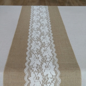 Puede incluir: Un camino de mesa de arpillera con un borde de encaje blanco. El encaje tiene un patrón floral.