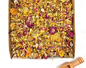 May include: A box filled with a mixture of dried yellow and pink flower petals. The petals are loose and scattered throughout the box. A small wooden scoop is next to the box.