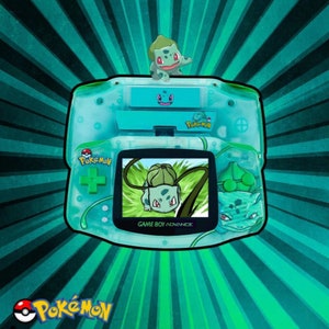 May include: A green Game Boy Advance SP console with a clear shell and a green Bulbasaur character on the top. The screen shows a green Bulbasaur character in a video game. The console has the words "Game Boy Advance" printed on the bottom.