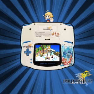Könnte beinhalten: Eine weiße und blaue Game Boy Advance Handheld-Spielkonsole mit einer blauen und weißen Final Fantasy Tactics Advance Spielkassette. Die Konsole hat ein blaues und weißes Design mit einem Bild von Charakteren aus dem Spiel auf der Vorderseite. Der Bildschirm zeigt eine Szene aus dem Spiel mit einem Gebäude und Charakteren im Schnee.