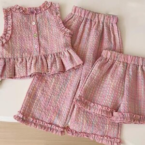Puede incluir: Un conjunto de tres piezas de tweed rosa, que incluye una blusa sin mangas con volantes, botones y un peplum, adem&aacute;s de pantalones cortos y pantalones a juego. La tela tiene un sutil patr&oacute;n de hilo multicolor.