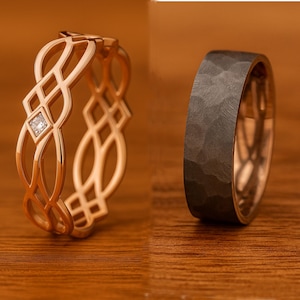 Könnte beinhalten: Zwei Ringe auf einer Holzoberfläche. Einer ist roségoldfarben mit einem durchbrochenen Design und einem kleinen quadratischen Diamanten. Der andere ist ein dunkelgraues, gehämmertes Metallband mit roségoldfarbenem Innen.