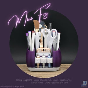 May include: A purple desk organizer labeled "Mini Fry" holds various craft tools, including scissors, pens, and a spatula. The organizer has a white base and silver accents. The text "Mini Fry" is in a cursive font.