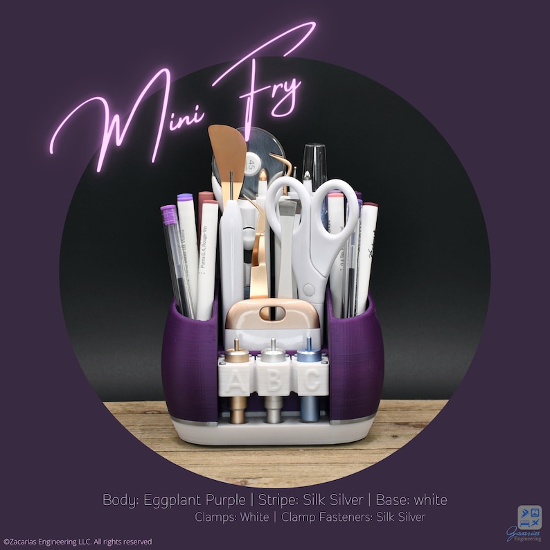 May include: A purple desk organizer labeled "Mini Fry" holds various craft tools, including scissors, pens, and a spatula. The organizer has a white base and silver accents. The text "Mini Fry" is in a cursive font.