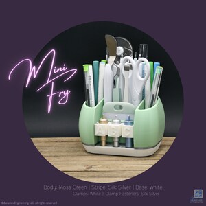 May include: A mint green desk organizer with the text "Mini Fry" in a neon pink script. The organizer holds various craft tools, including scissors, pens, and small bottles labeled A, B, and C. The base is white, and the accents are silver.