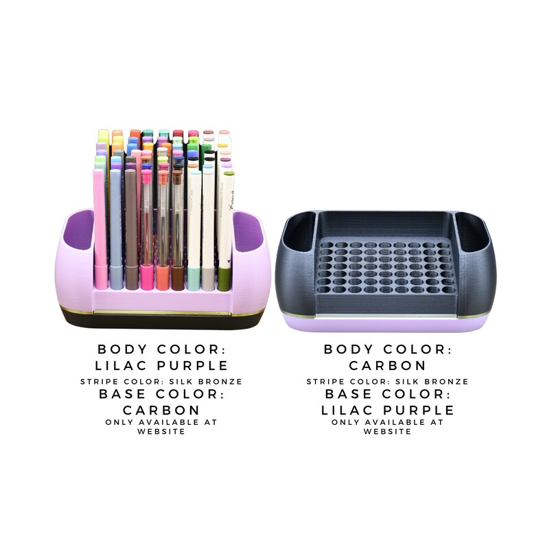May include: Two pen holders, one lilac purple and one carbon. The lilac purple holder contains various pens. Both holders have a silk bronze stripe and a carbon or lilac purple base. Text on the image indicates availability on the website.