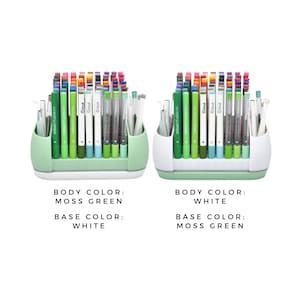 May include: Two pen holders, one with a moss green body and white base, the other with a white body and moss green base. Each contains various coloured pens and markers, including Cricut brand pens. The image text indicates the body and base colours.