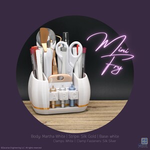 May include: A white and gold craft organizer filled with various tools, including scissors, pens, and spatulas. The organizer has three compartments and a base with gold accents. The text "Mini Fry" is written in a neon style.