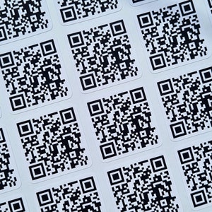May include: A sheet of white paper with multiple black and white QR code stickers.