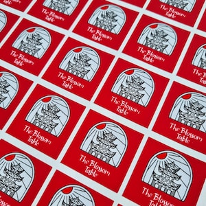 May include: A sheet of red square stickers with a white pagoda-like building design and the text "The Blossom Table" repeated on each sticker.