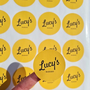 May include: A sheet of yellow round stickers with the text "Lucy's Bakery" in black script font.
