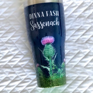 May include: A blue and green tumbler with a glitter finish. It features a thistle design and the text "Dinna Fash Sassenach".