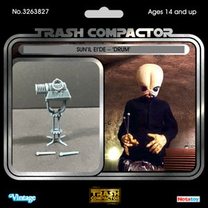 Op de afbeelding: Vintage actiefiguurverpakking met een grijs drumstel en een figuur van Sun'il Ei'de, met het label 'Drum'. De verpakking bevat de tekst 'TRASH COMPACTOR' en 'Ages 14 and up'.