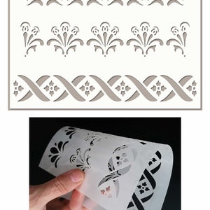 May include: A white plastic stencil featuring three different designs. The top design is a row of five simple floral shapes. The middle design is a row of five more elaborate floral shapes. The bottom design is a repeating pattern of interlacing lines with small floral shapes.