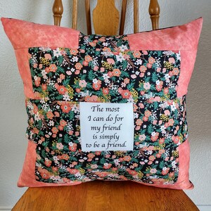 May include: Square decorative pillow with a floral pattern in shades of orange, pink, and white on a black background. The pillow has a coral border and a white square with the text: "The most I can do for my friend is simply to be a friend."
