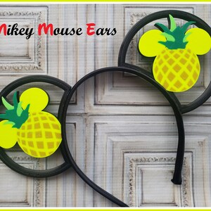 May include: Black Mickey Mouse ears headband with yellow and green pineapple designs. The pineapple has a brown textured pattern.
