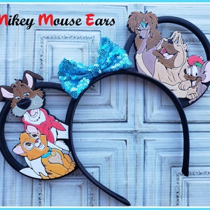 May include: Mickey Mouse ears headband with a blue sequin bow and a 3D image of characters from the film The Lady and the Tramp. The characters include Lady, Tramp, and Jock.