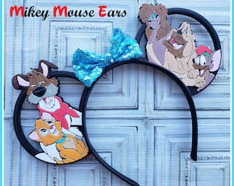 Op de afbeelding: Mickey Mouse orenband met een blauwe pailletten strik en een 3D-afbeelding van personages uit de film Lady en de Vagebond. De personages zijn Lady, Tramp en Jock.