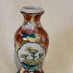 May include: A small, yellow and red porcelain vase with floral designs. The vase has a black base and is decorated with gold accents.