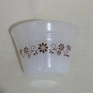 Op de afbeelding: Witte keramische mengkom met een bruin bloemenmotief. De kom heeft een gegolfde rand en de woorden "Pyrex" staan ​​gedrukt op de bodem.