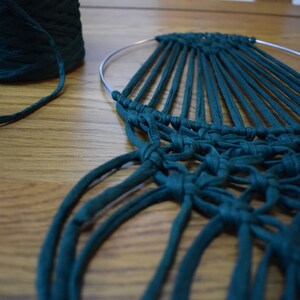 K&ouml;nnte beinhalten: Ein t&uuml;rkisfarbener Makramee-Wandbehang mit einem runden Metallring und langen Garnstr&auml;ngen, die herunterh&auml;ngen.