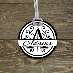May include: A round luggage tag with a black and white design. The tag features a stylized letter "A" with a decorative flourish and the name "Adams" printed in a script font.