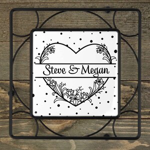 May include: Black and white heart-shaped pot holder with the text "Steve & Megan" in a decorative font. The heart is surrounded by a floral design and a white background with black polka dots.
