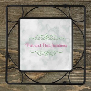 May include: Black metal trivet with a white square tile insert. The tile has a green and white watercolor background with a green decorative flourish and the text "This and That Solutions" in pink.