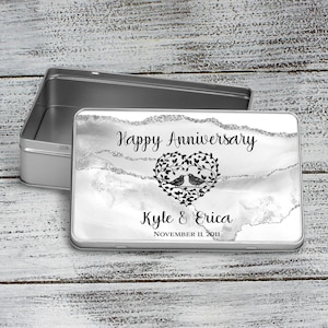 May include: Silver tin box with a white and gray marble design. The box has a black heart with two birds inside and the text "Happy Anniversary Kyle & Erica November 11, 2011".