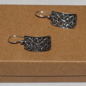 May include: A pair of silver earrings with a delicate floral design. The earrings are on a brown background.