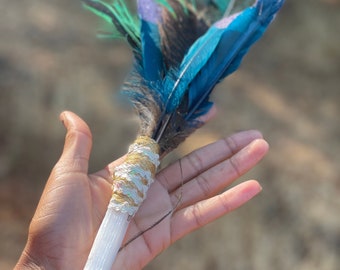 May include: A white selenite wand wrapped in gold and white string with a bundle of blue, green, and brown feathers attached to the top.