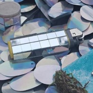 May include: A silver lighter with a mirrored surface and a black plastic handle. The lighter is lying on a bed of iridescent sequins.