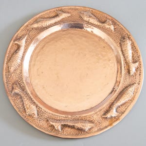 May include: A round copper serving tray with a hammered finish and a raised design of fish around the edge.